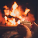Cup of tea in woman's hands sitting near fireplace